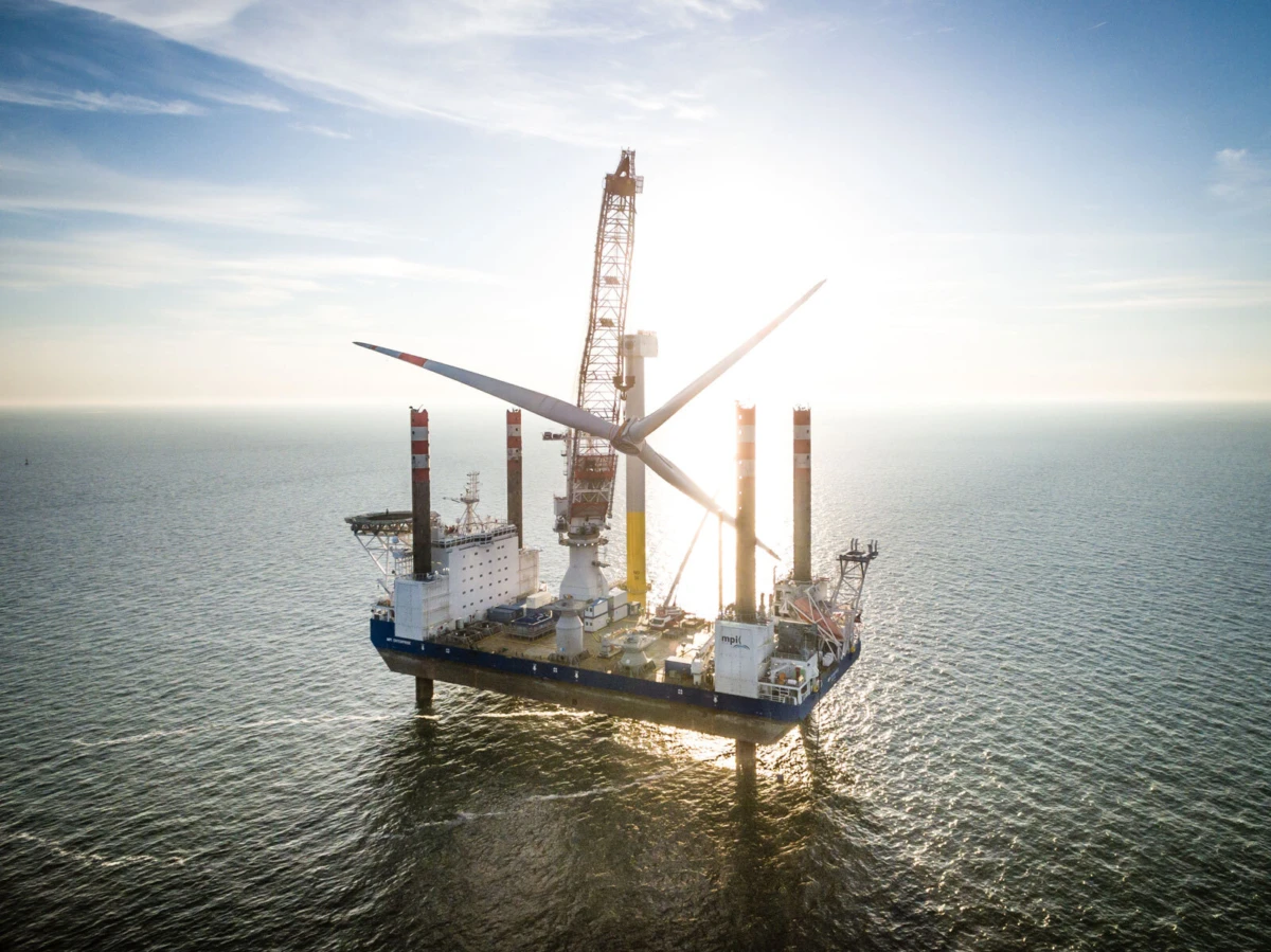 Offshore jack-up drilling rig with a wind turbine on its deck at sunset.