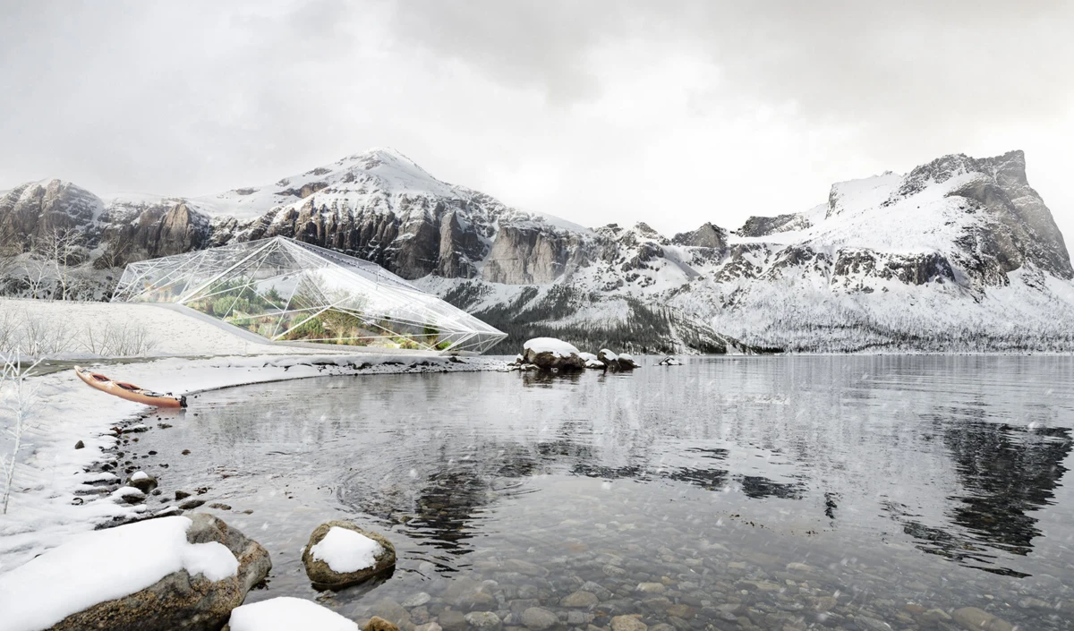 Geodesic glass greenhouse on a snow-covered lakeshore with a small orange kayak nearby; snow-capped mountains in the background.