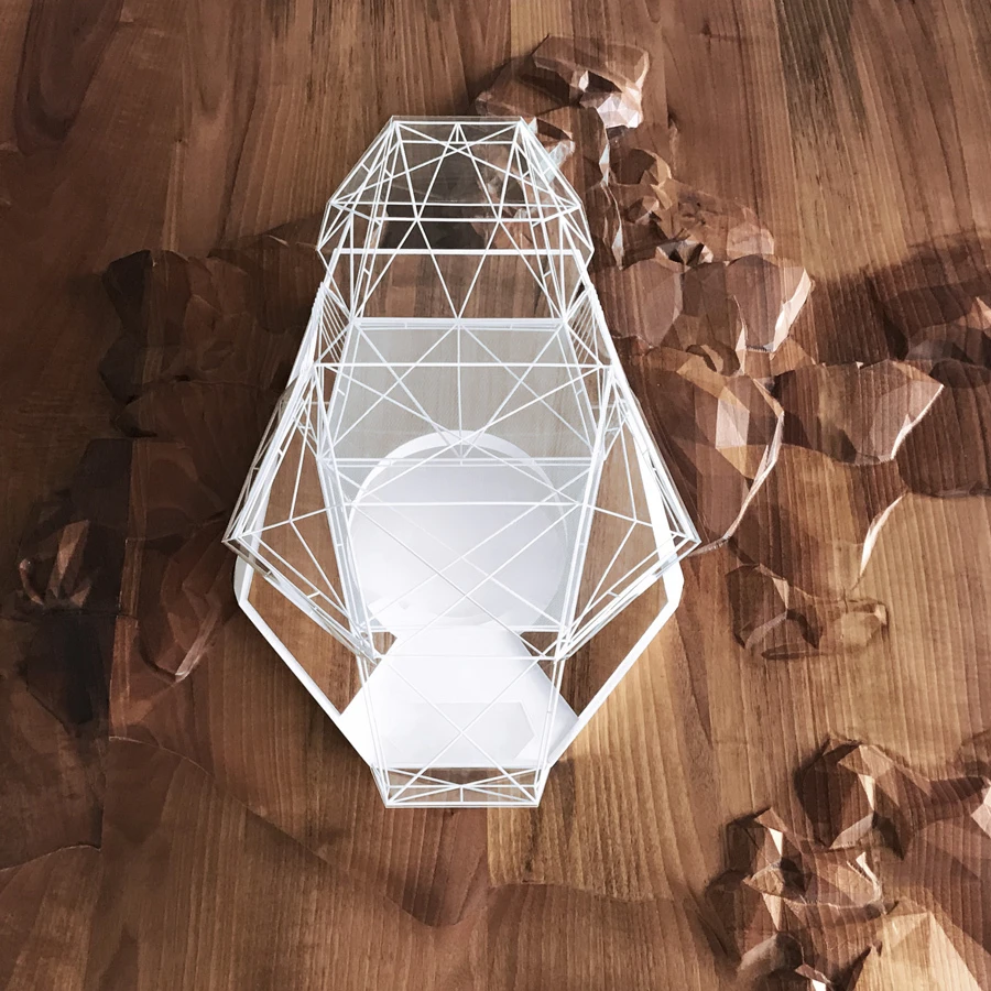Geometric white wireframe lantern sculpture on a wooden surface with crumpled brown paper around