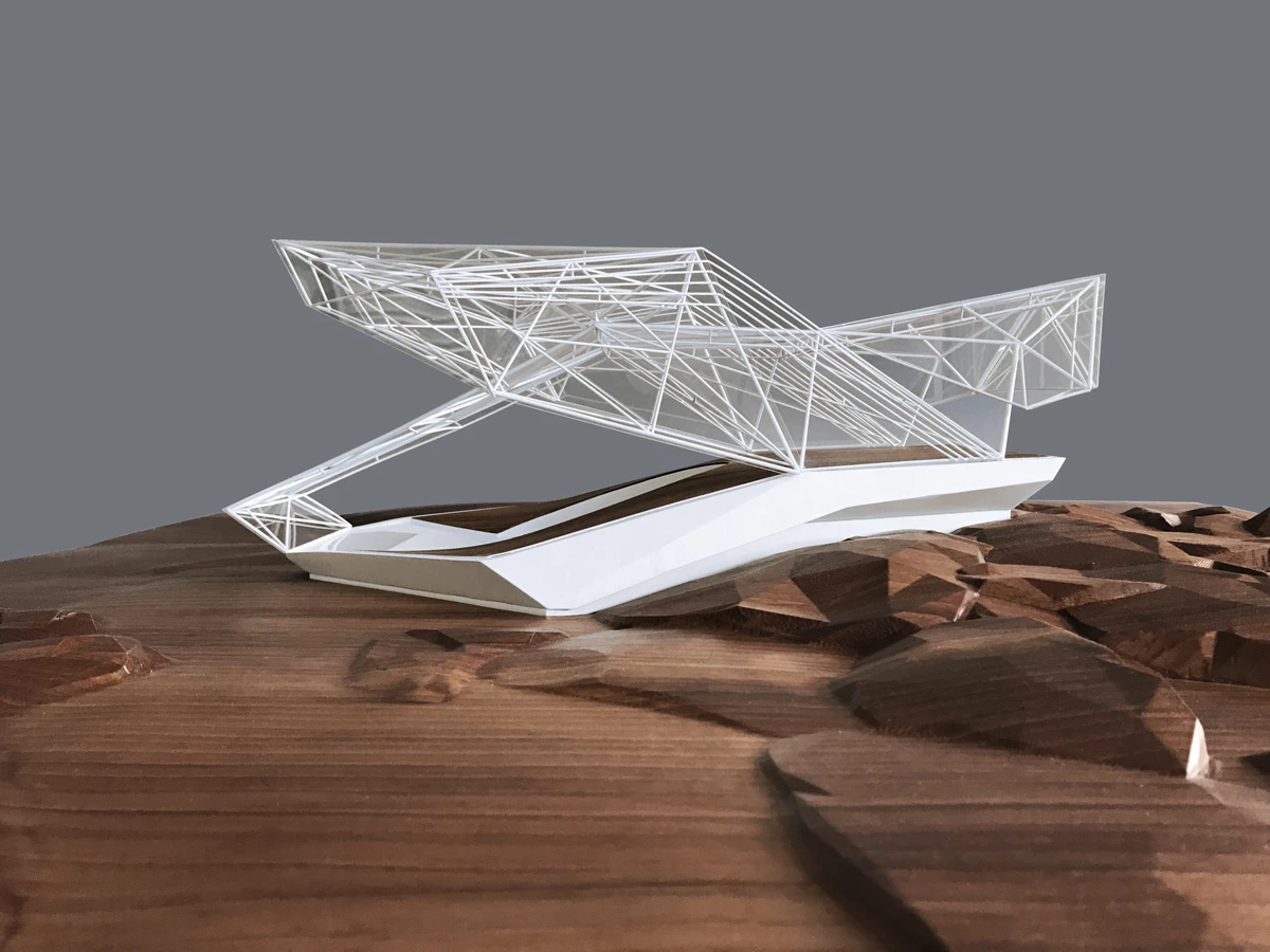 White geometric wireframe architectural model perched on a rocky brown surface against a gray backdrop.