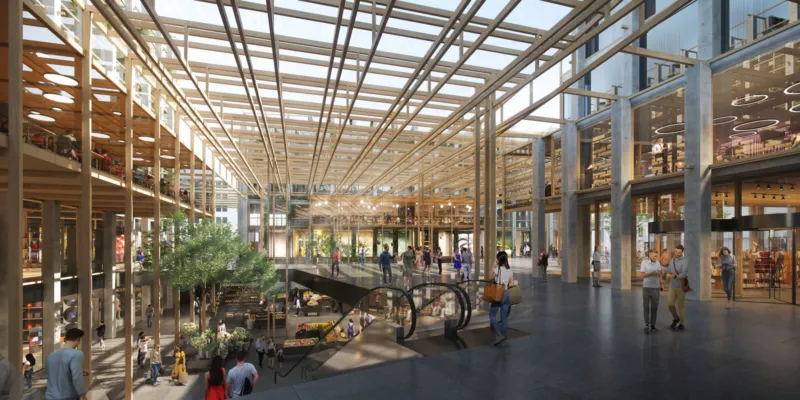 Shoppers walk through a bright, multi-level shopping mall atrium with escalators and a glass roof.