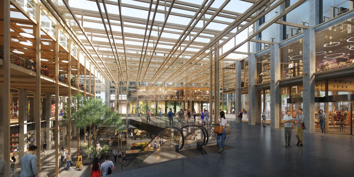 Shoppers walk through a bright, multi-level shopping mall atrium with escalators and a glass roof.