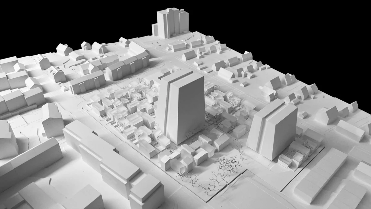 Aerial view of a 3D white architectural model of a city block with two tall rectangular buildings among low-rise houses, streets and trees.