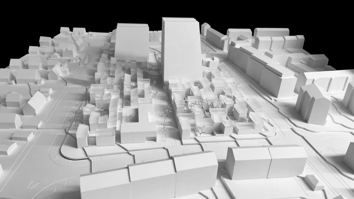 White architectural scale model of an urban district, featuring a tall central building among clustered blocks and network of streets.