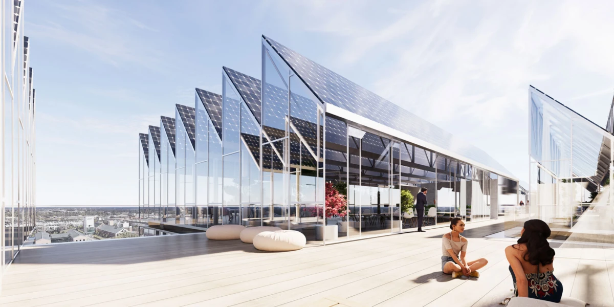 Two women sit on a wooden rooftop deck beside a glass-walled zigzag-roofed modern building, chatting as cityscape stretches behind.