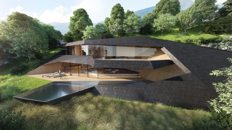 Person standing on a wooden deck of a modern angular hillside house with glass walls beside a reflecting pool, surrounded by trees.