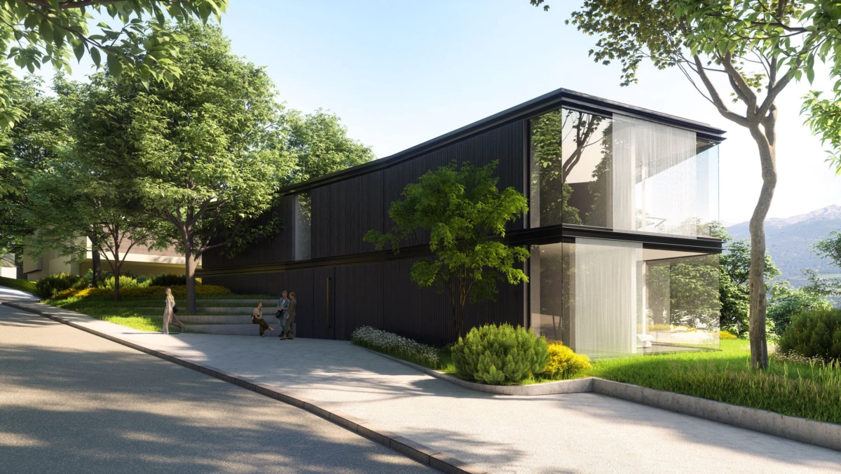 Modern two-story black glass house with large windows; two people stand near the entrance on a sunlit walkway among trees.