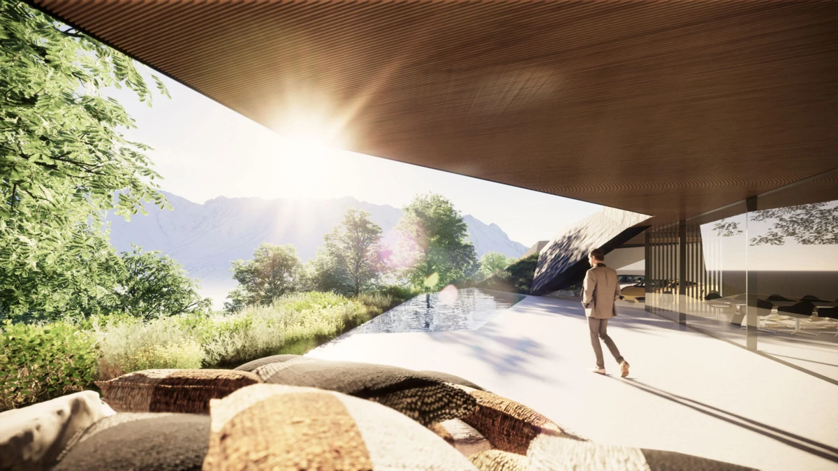 Person walking on a sunlit patio beside a reflecting pool, under a large overhanging roof of a modern building, with mountains and trees beyond.