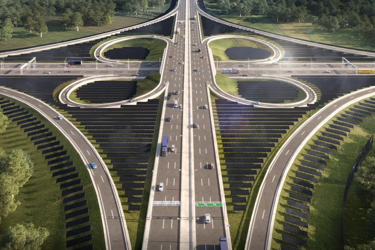 Aerial view of a complex highway interchange with looping ramps, cars traveling along multiple lanes, surrounded by greenery and solar panels.