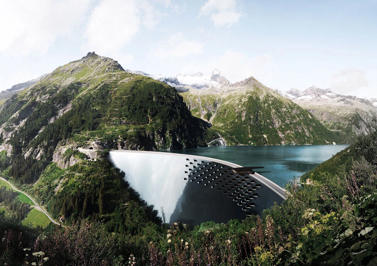Curved concrete dam across a turquoise alpine lake, surrounded by green mountains and distant snow-capped peaks.