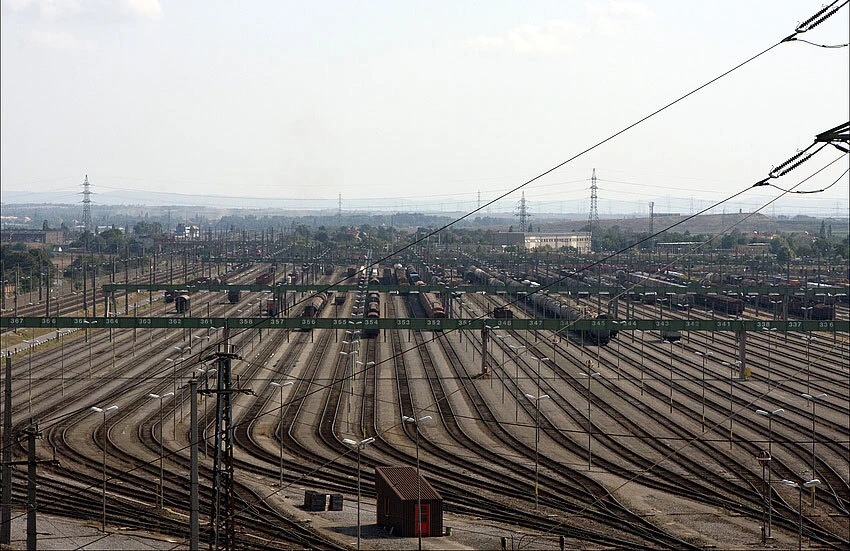 Vast railway yard with many parallel tracks filled with freight cars and overhead power lines.