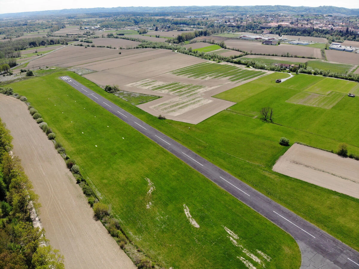 Aerial view of a narrow asphalt runway crossing vibrant green farmland and brown plowed fields in a rural landscape.