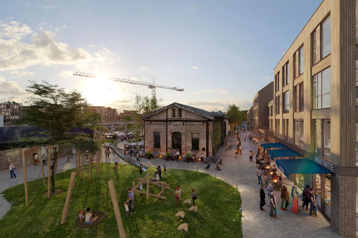 People socialize and stroll in a lively urban plaza around a brick industrial building; playground and modern storefronts at sunset.