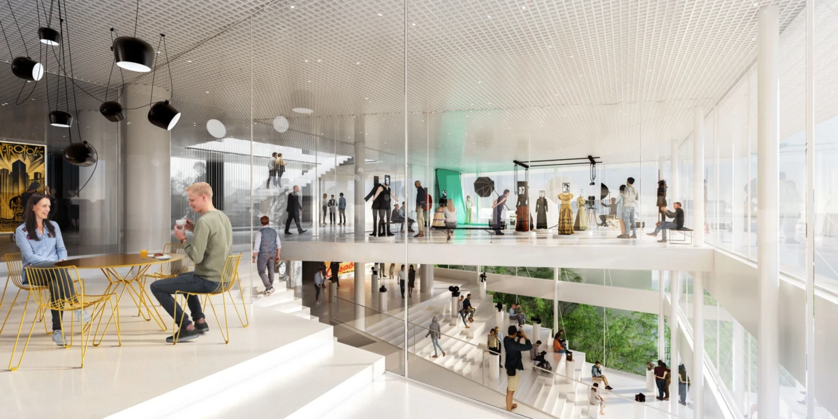 Bright glass-walled, multi-level gallery with fashion mannequins on an upper display; visitors walk and chat; yellow cafe seating on lower level.