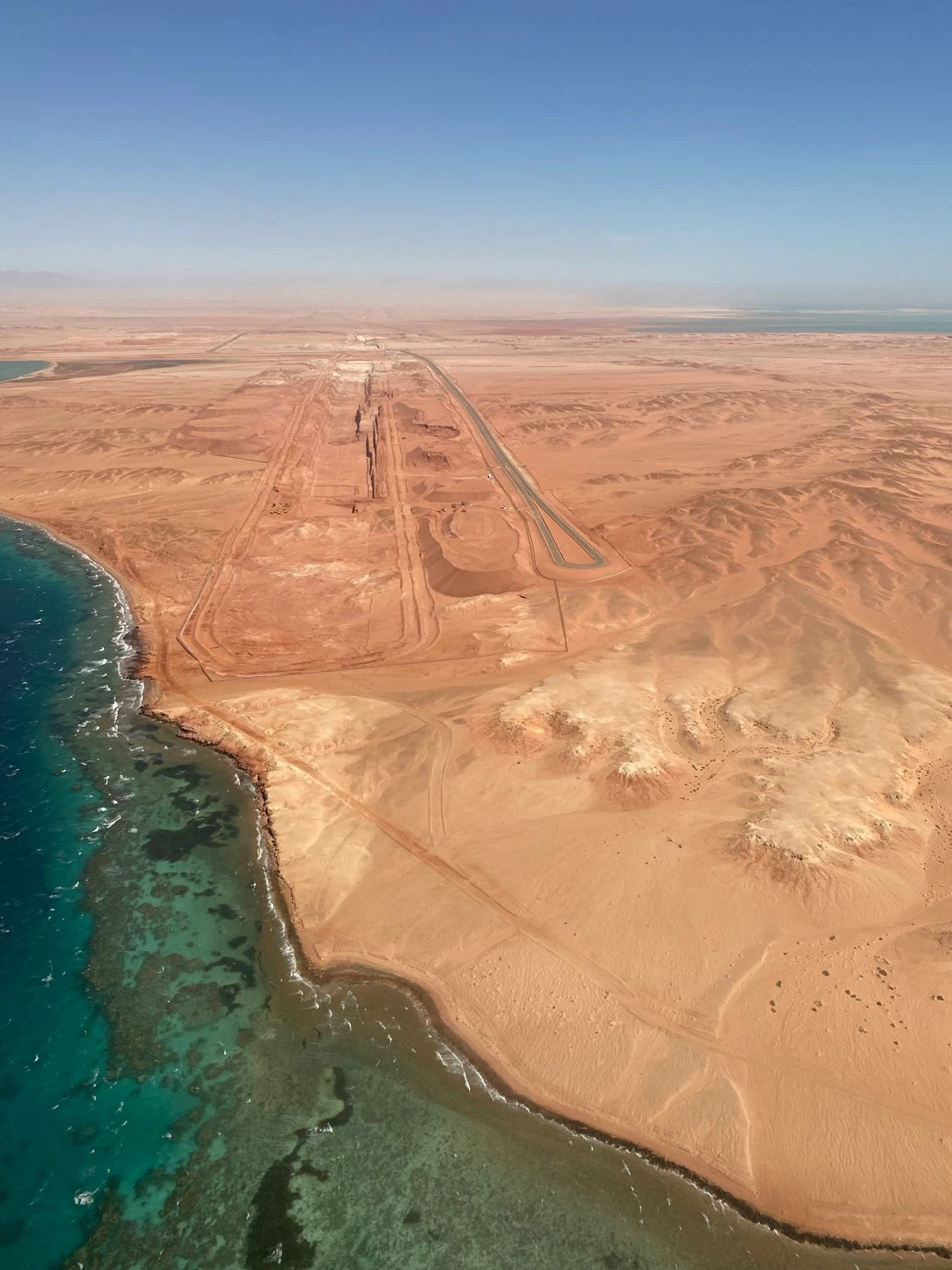 Aerial view of a desert coastline with an elongated airstrip and road grid.