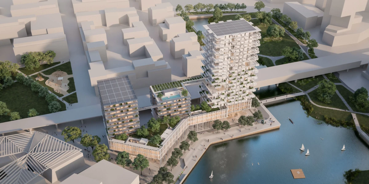 Modern waterfront mixed-use complex with a tall residential tower with solar panels on the roof, linked to low-rise buildings beside a river.