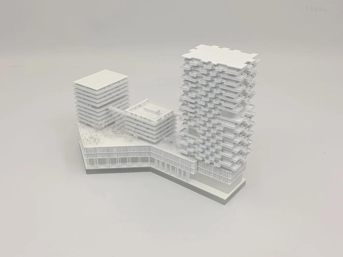 White architectural scale model of a modern urban complex: a tall stacked-tower, a shorter block tower, and a connecting bridge on a white base.