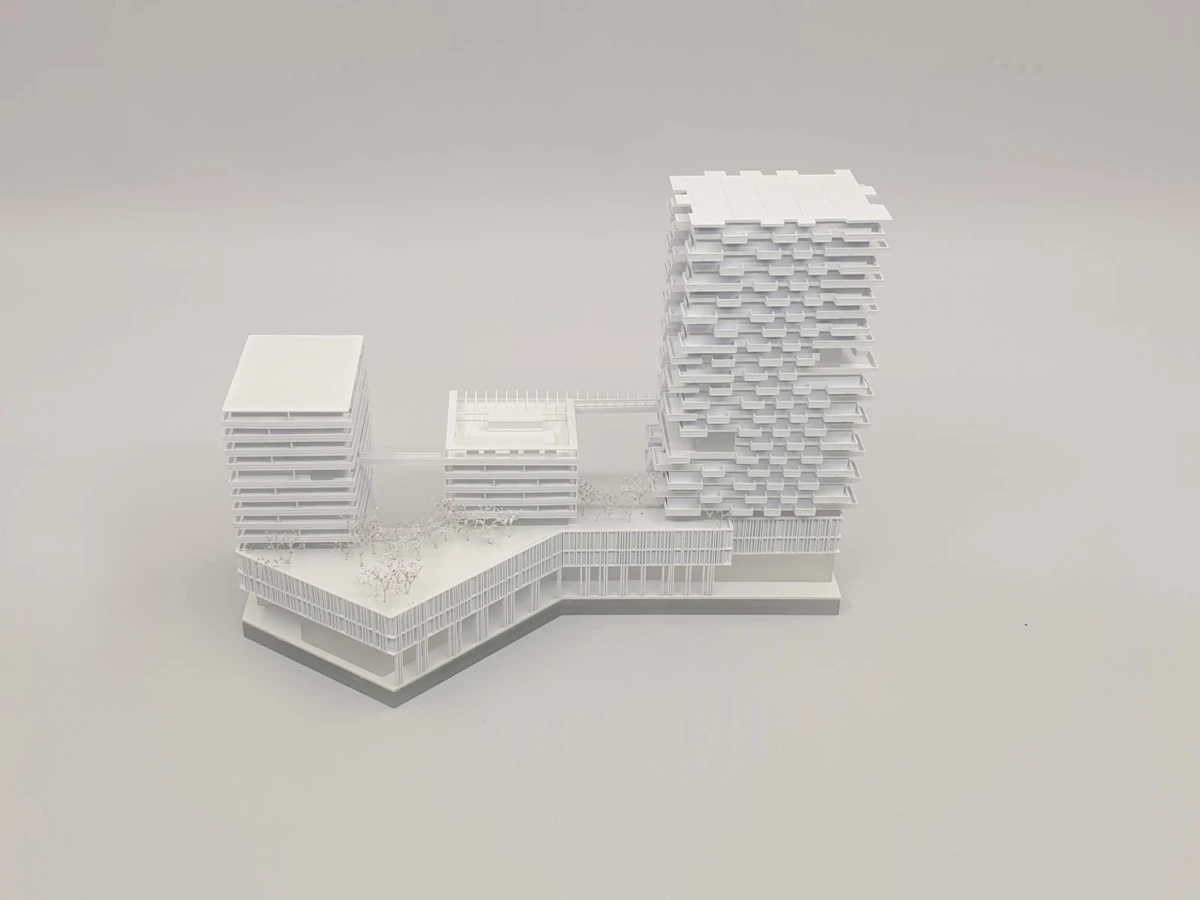 White architectural scale model of a modern building complex with a tall stacked high-rise and a mid-rise block connected by bridges.