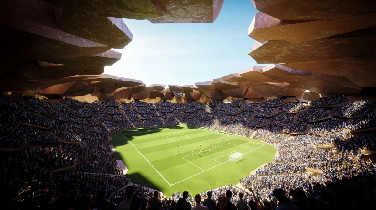 Soccer match in a packed stadium with a green field, players near the goal, under a massive rock-like roof opening to the blue sky.