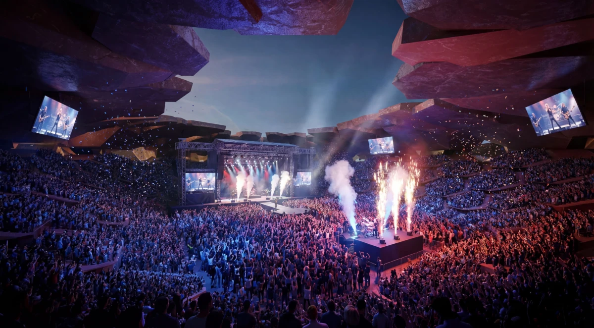 Massive arena concert: a band performs on a lit stage with pyrotechnics as a dense crowd fills the venue.
