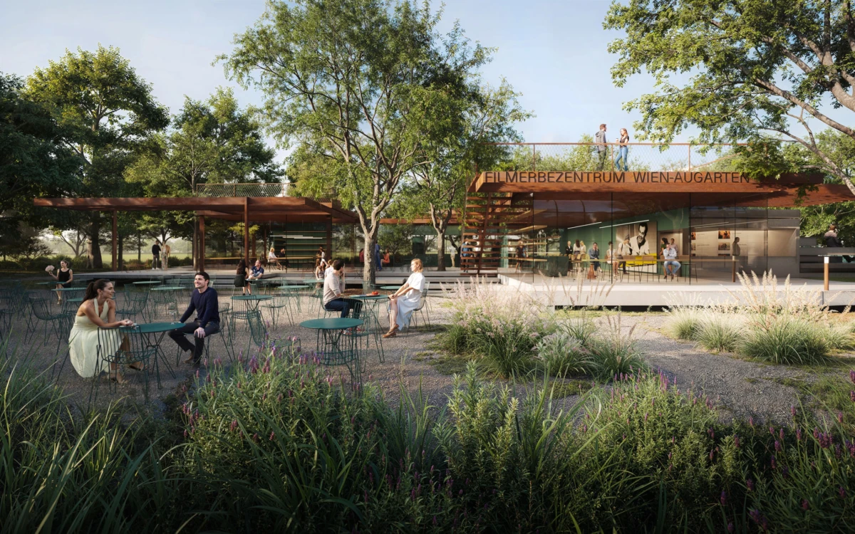 People sit and chat at green metal tables in a landscaped plaza beside a modern cinema center with trees.