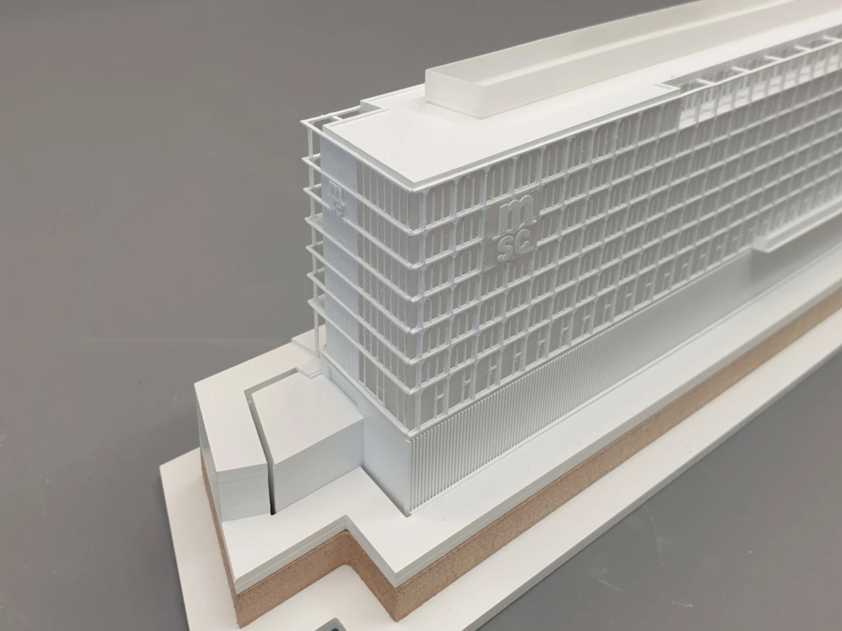 White architectural scale model of a modern high-rise office building with vertical louvers on a stepped display base.