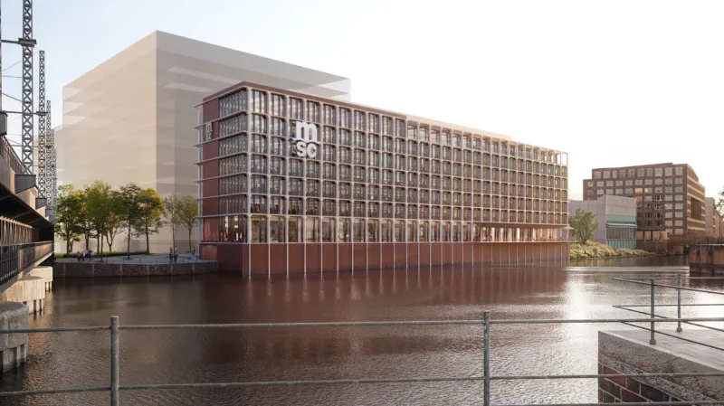 Glass-and-brick office building on a riverfront, with a tree-lined promenade and distant urban blocks.