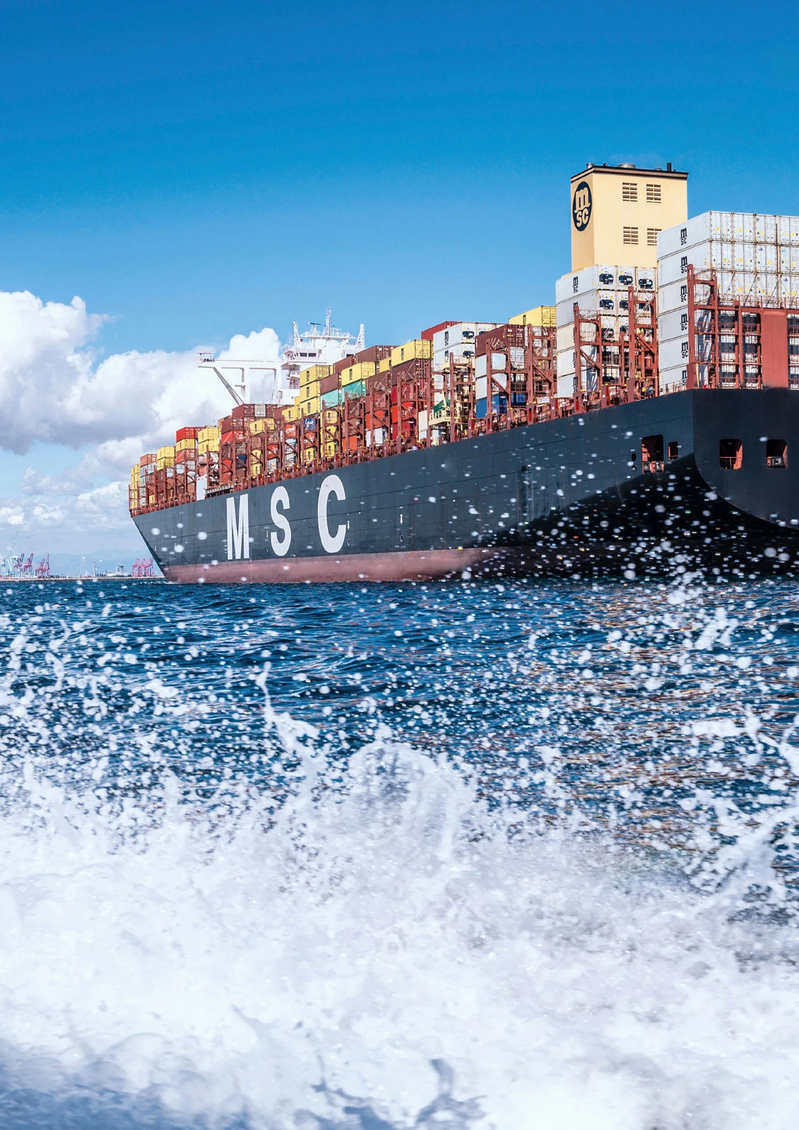 MSC container ship at sea with stacked colorful containers; waves splashing in the foreground.