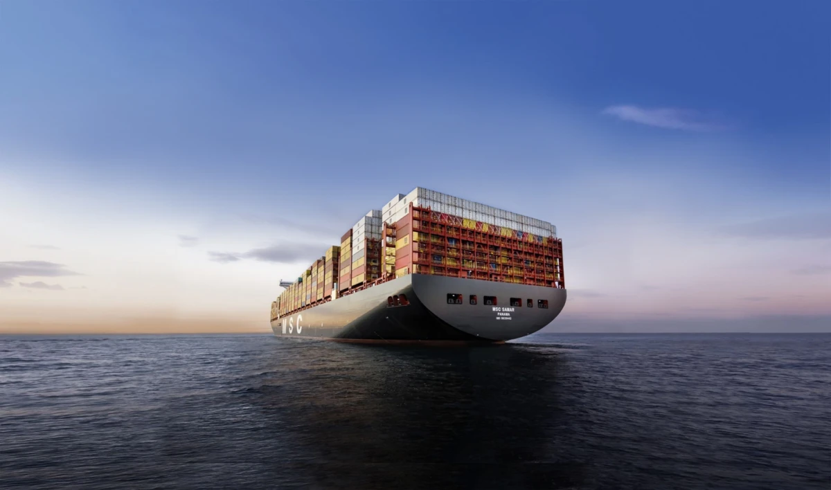 Large container ship sailing on calm sea with stacked shipping containers at sunset.