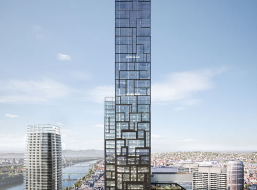 Tall glass skyscraper with a modular, lattice-like façade rises above a city by the river, among other high-rises under a clear blue sky.