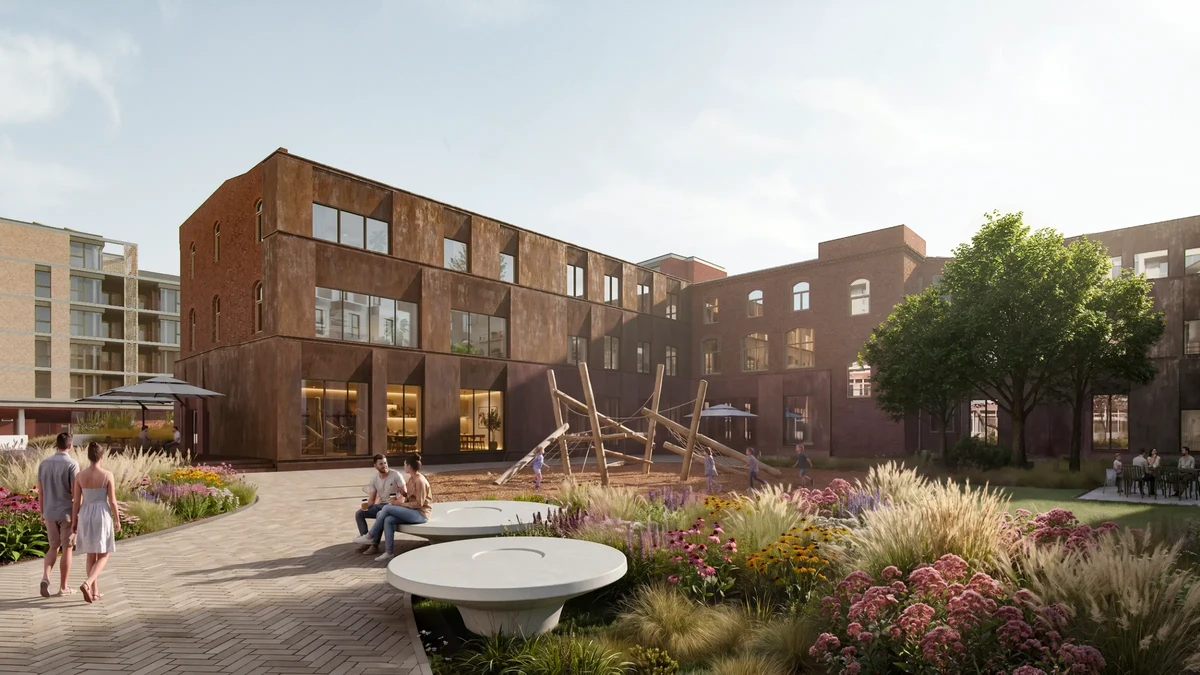 Public courtyard with a brown-brick building, a wooden sculpture, and people strolling and sitting among flowering plants.