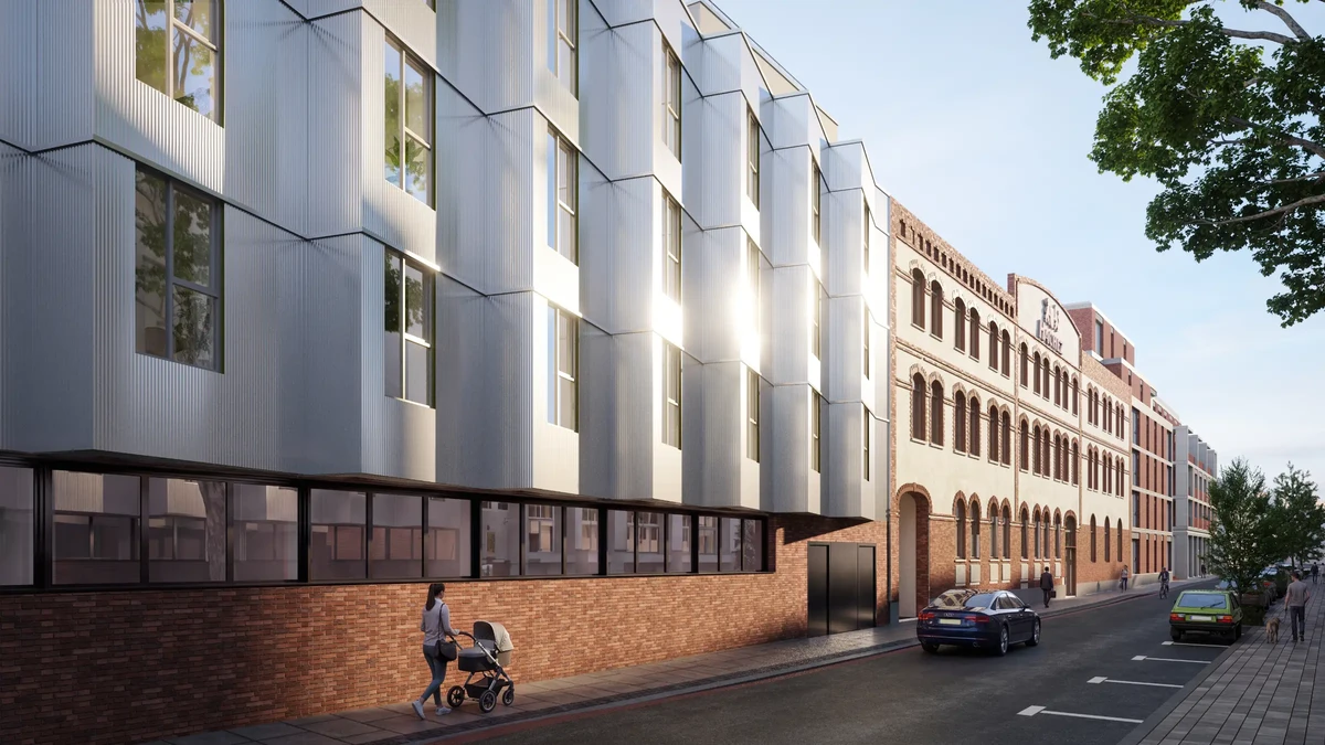 Urban street featuring a modern gray metal-clad building beside a brick historic facade; a person pushes a stroller, with cars parked along the road.