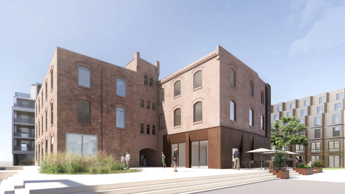 Two brick buildings with arched windows flank a paved urban plaza; pedestrians walking near storefronts and an outdoor cafe.