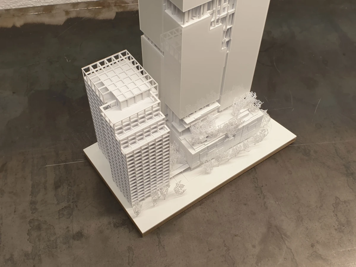 White architectural scale model of a city block with tall modern buildings, trees, and landscaping on a display base.