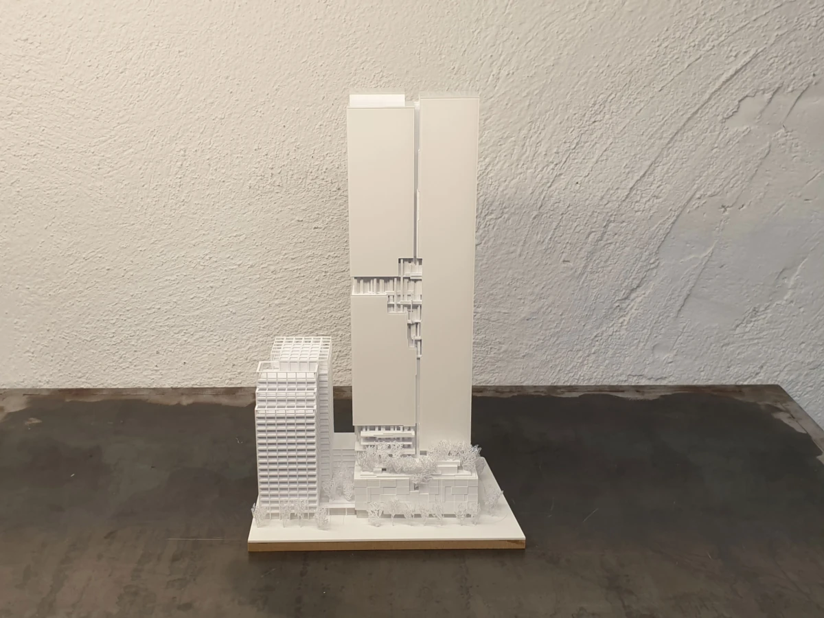 White architectural scale model of a modern high-rise complex, featuring a tall central tower and a curved-front building on a display base.