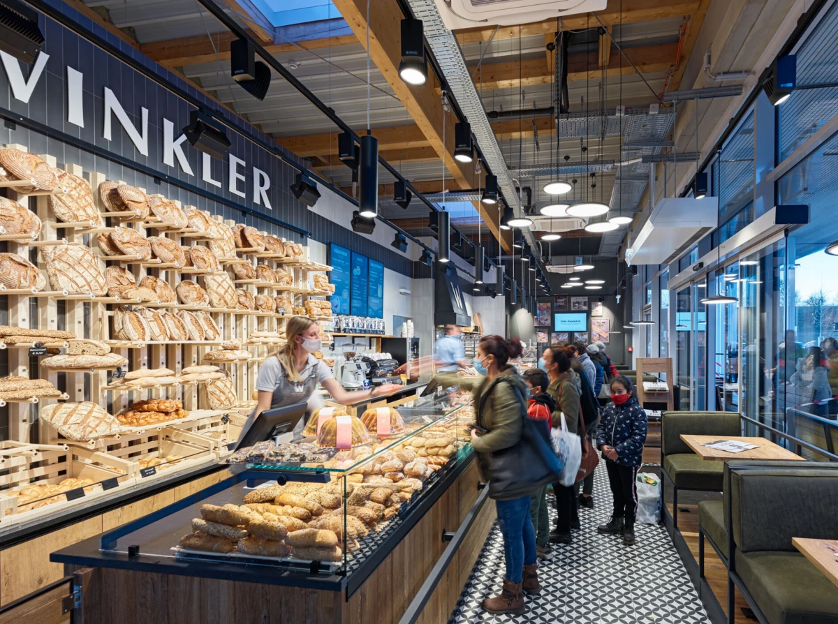 Bakery interior with shelves of loaves, glass display case of pastries, staff at the counter serving customers; prominent sign reads VINKLER.