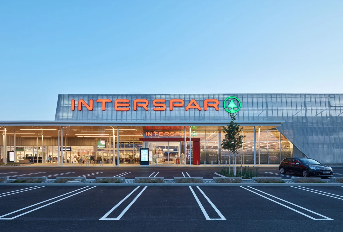 INTERSPAR supermarket exterior with glass facade and illuminated sign; parking lot in foreground with a car.