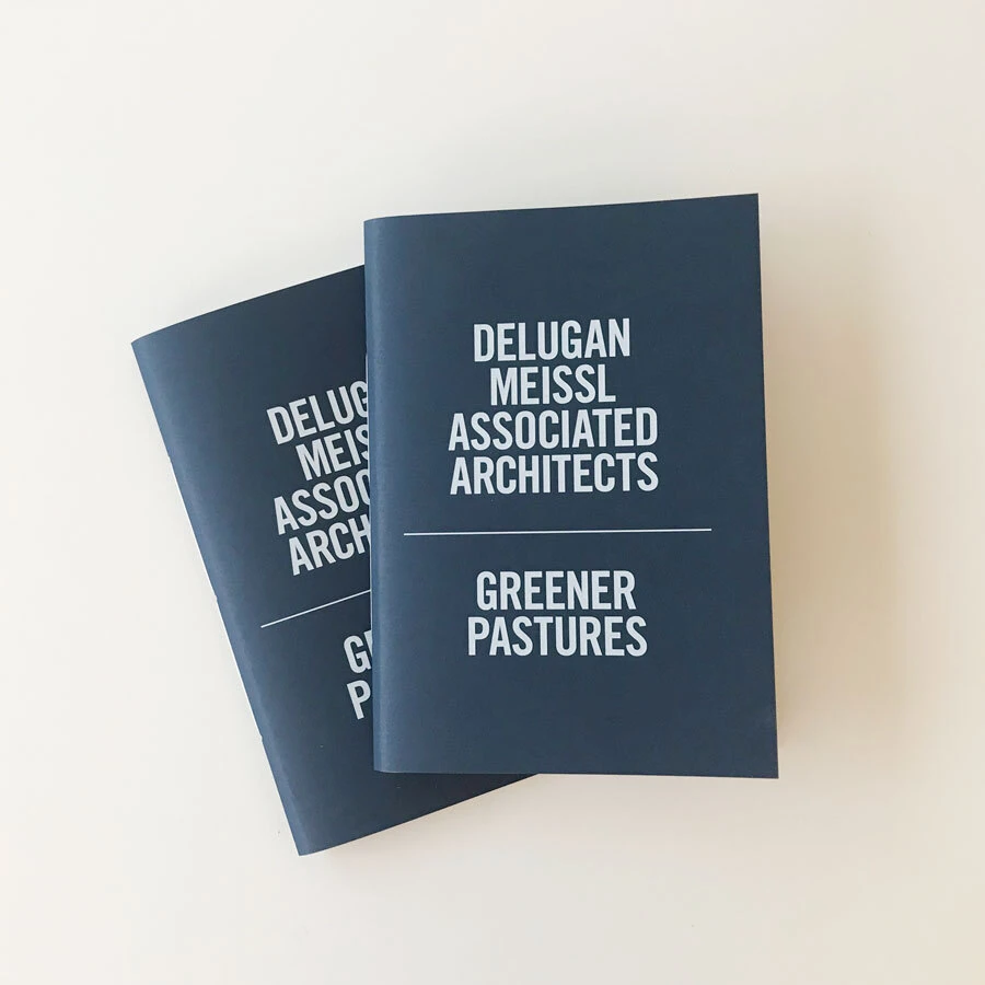 Two dark blue booklets with white text reading Delugan Meissl Associated Architects and Greener Pastures on a white background