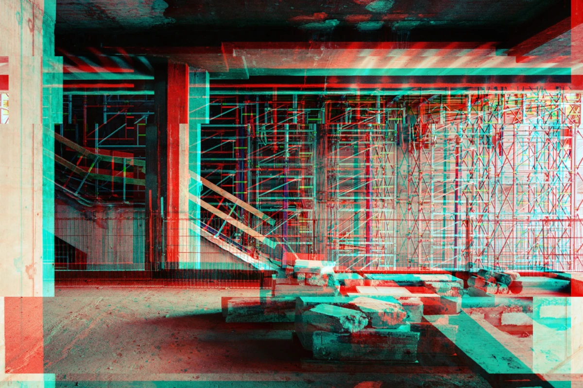 Interior construction site with steel scaffolding, wooden planks, and scattered concrete blocks.