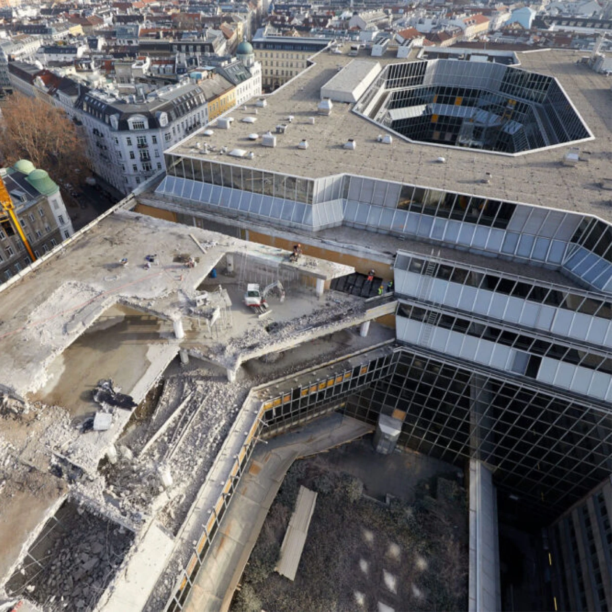 Aerial view of a rooftop construction site on a glass-clad building; rubble, a partially collapsed concrete platform, and workers with a truck.