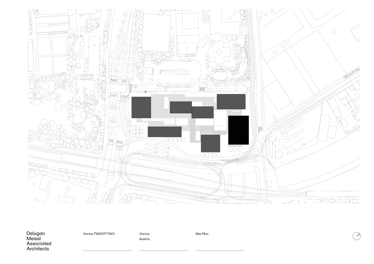 Aerial site plan of a modern architectural complex with dark rectangular volumes arranged around a central courtyard, surrounded by roads and trees.