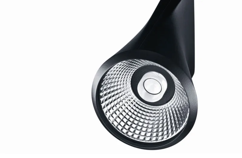 Close-up of a circular LED spotlight head with a faceted reflector on a black curved arm against a white background.